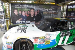LGH leadership team banner behind our sponsored NASCAR race car