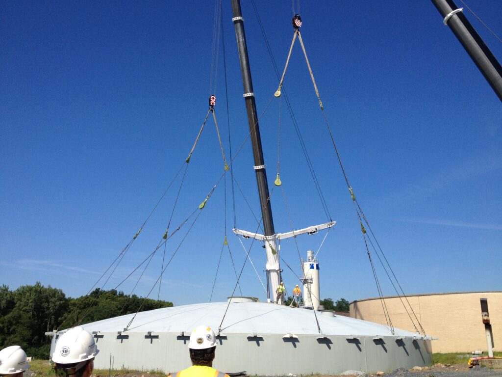 Snatch block rigging, including slings under a crane, being used to lift the dome of a water tank.