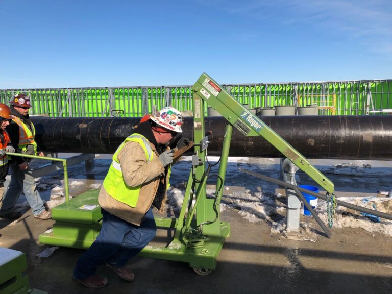 a couple of construction workers dressed in safety gear push a hydraulic floor portable crane