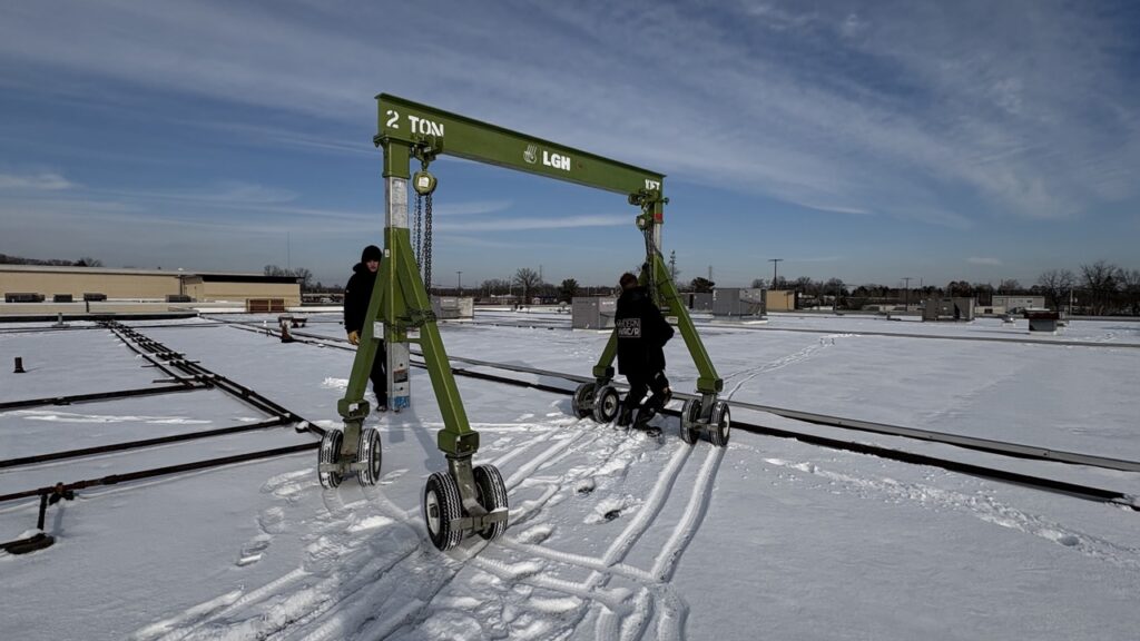 An aluminum gantry crane on pneumatic casters, being pushed across a snowy roof top