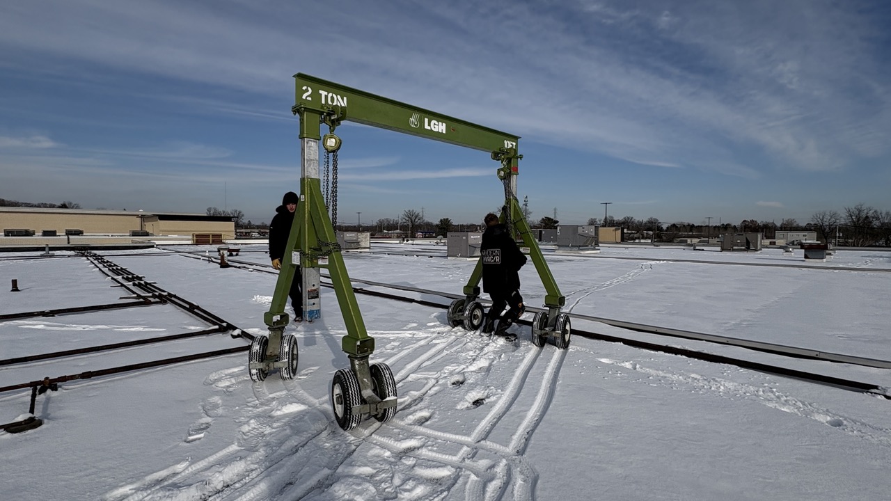 An aluminum gantry crane on pneumatic casters, being pushed across a snowy roof top